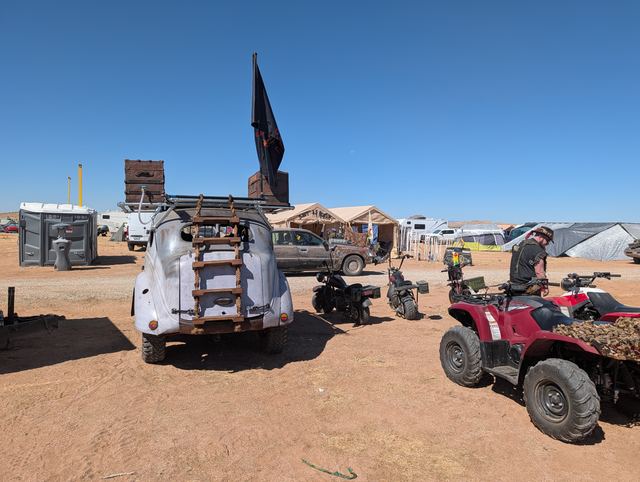 The back of the war car with a ladder to the roof rack, a red quad parked beside it.