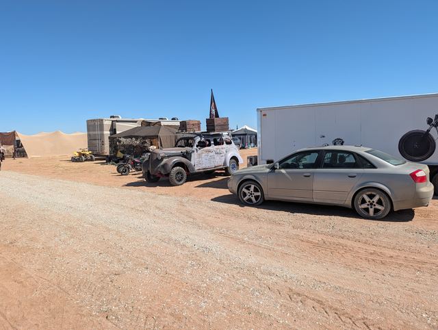 A camp lane with the war car and a modern sedan parked side by side.
