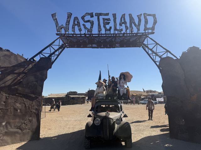 The war car driving under the Wasteland gate with riders on the roof.