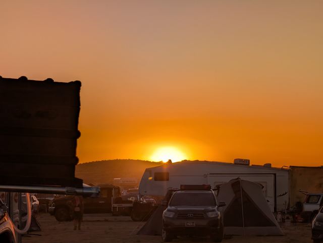The sun setting over campers and trailers, a dark shack silhouetted on the left.