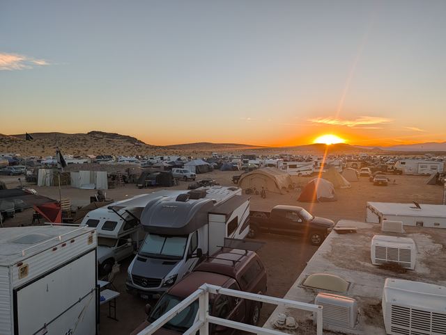 Sun rising over the far ridge behind rows of RVs and trailers.