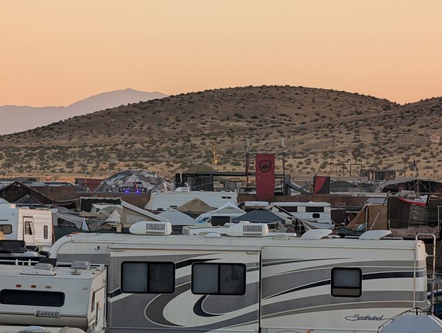 RVs and trailers parked beneath a scrubby hill washed in pink evening light.