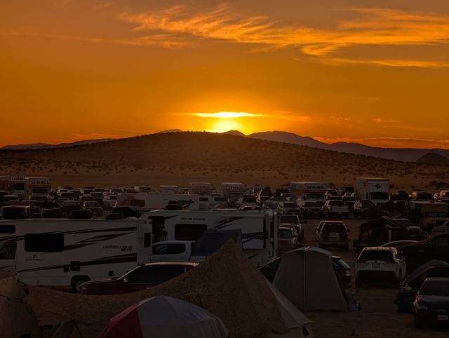 The sun sinking into a ridge beyond rows of campers, the sky burning orange.