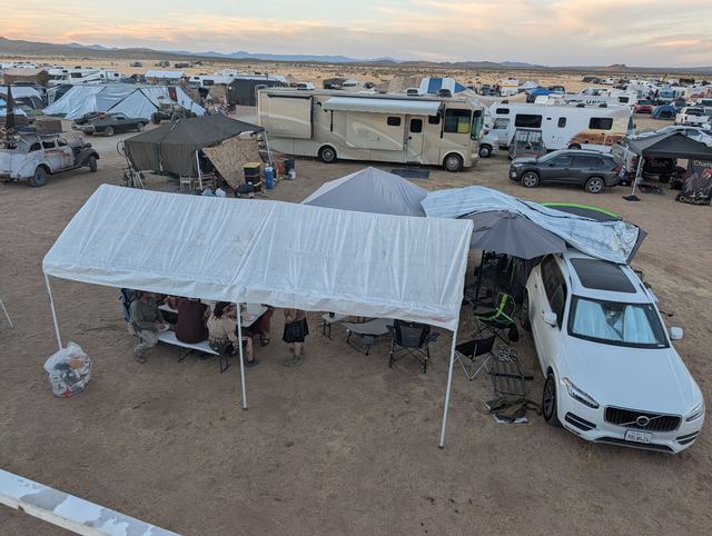 The tribe camp from above: white canopies, chairs and a white SUV.