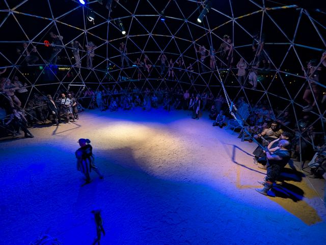 Two fighters on the bright sand floor of the Thunderdome under spotlights.
