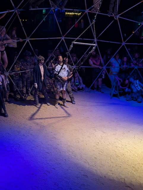 The dome floor with fighters at the far edge, spotlights pooling on the sand.