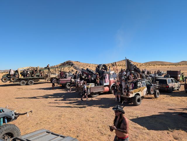 A long row of convoy vehicles and riders on the desert flats under a cloudless sky.