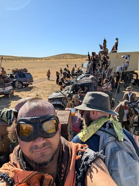 Selfie of a goggled rider on top of a war rig with the convoy behind.