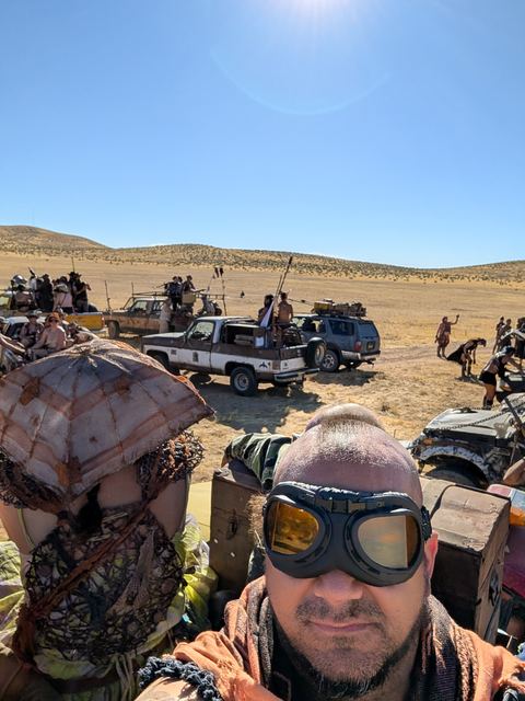 Riders in goggles and woven hats atop a vehicle, the convoy stretching behind.