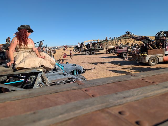 A rider in a wide hat sits atop a rusted war rig on the flats.