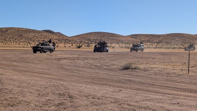 Convoy vehicles crossing the wide desert flats toward distant hills.