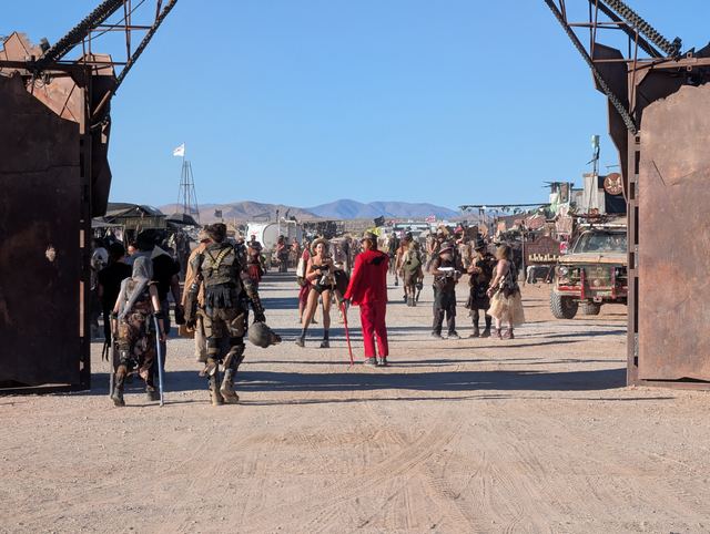 A crowd of costumed wastelanders passing through the town gate.