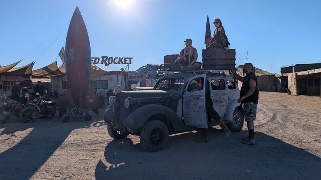 The war car with a rider on its roof beside the Red Rocket sculpture.