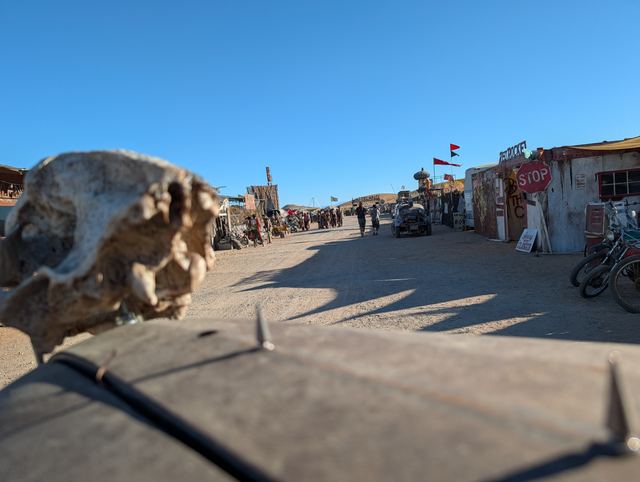 A fanged skull hood ornament leading the war car down a busy street.