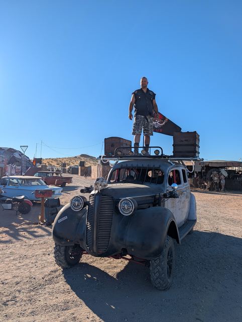 Low angle of the rooftop rider on the war car against a deep blue sky.