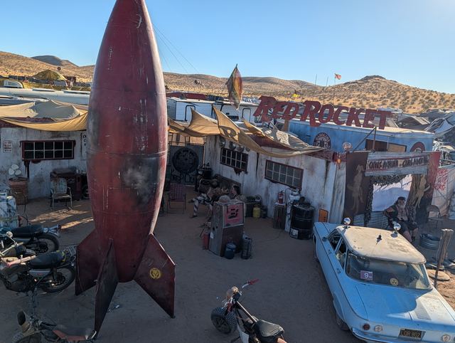 Rooftop view of the Red Rocket sculpture, motorcycles and a vintage blue car below.