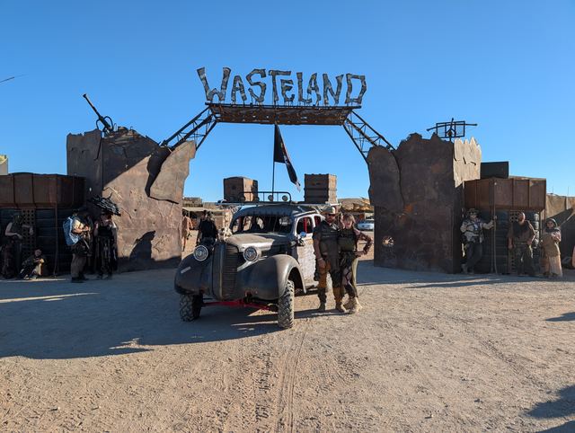 The war car under the gate, riders on top and people around it.