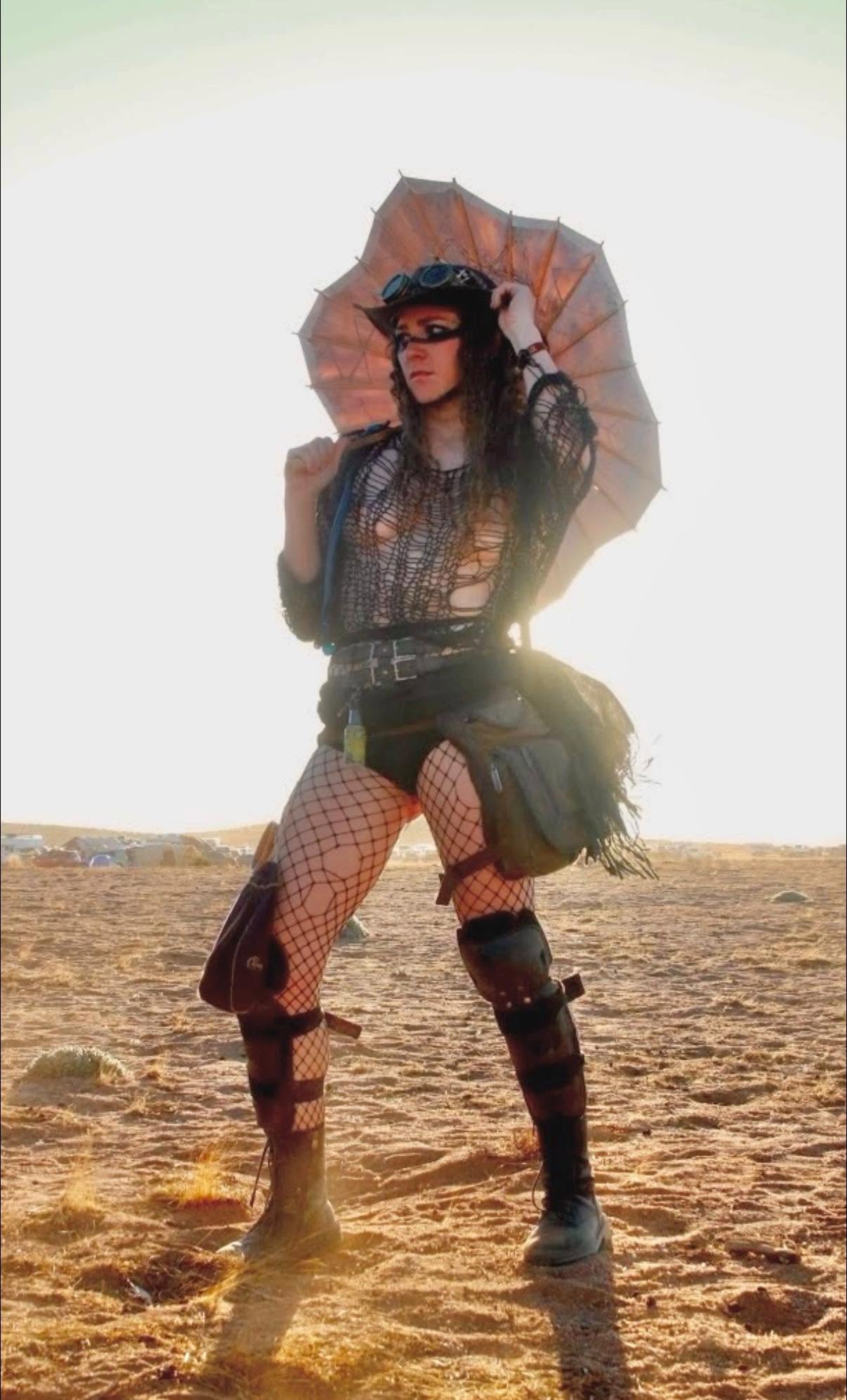 Sweet Tooth poses in the desert backlit by the sun, holding a tattered parasol, in goggles, fishnets, and armored boots.