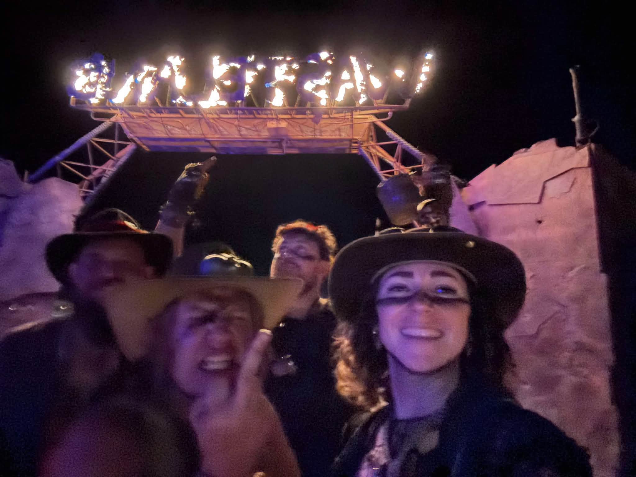 A blurry night selfie of five grinning members under the burning WASTELAND sign.