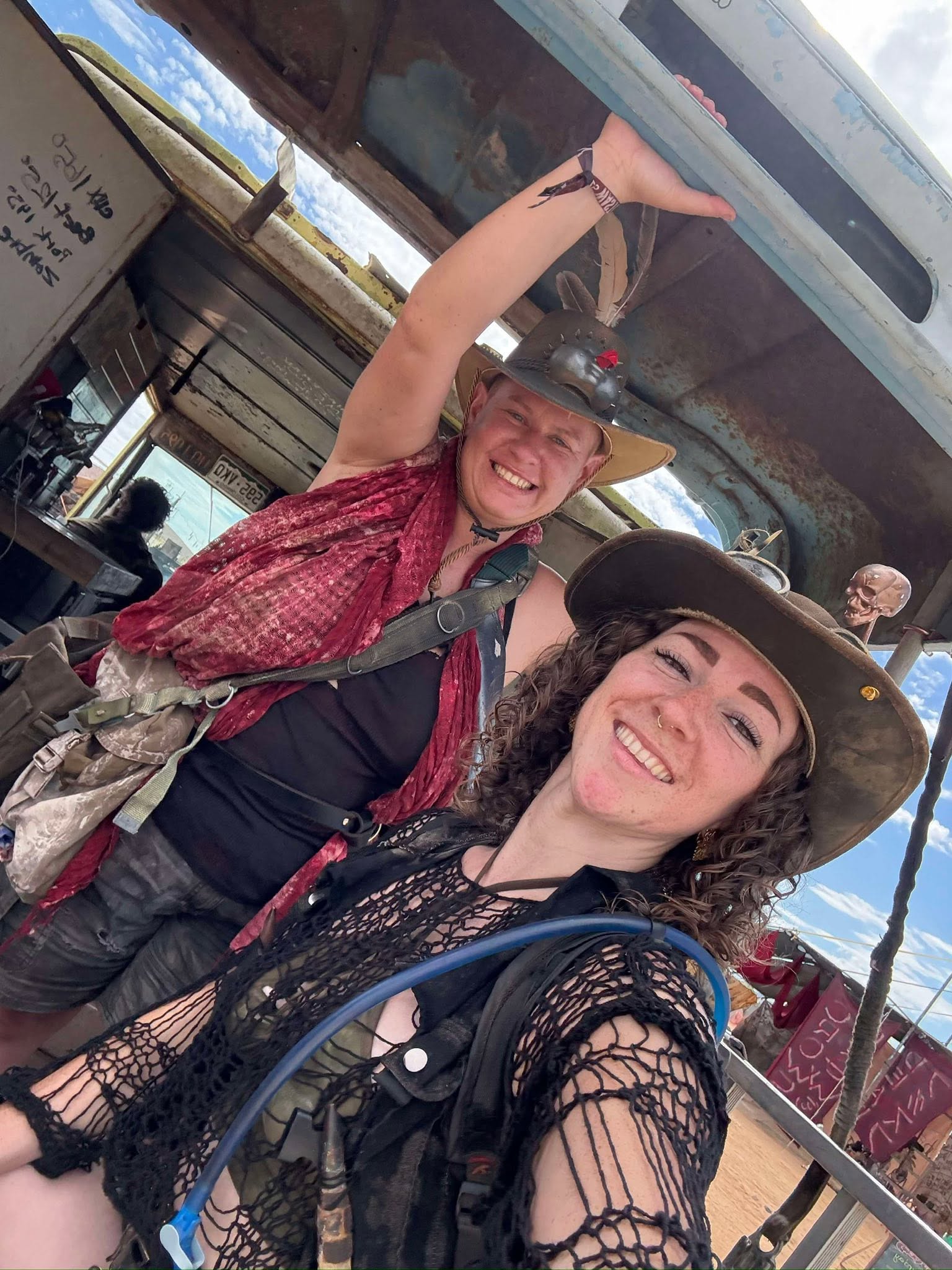 The same two members under the rusted truck, a skull-topped pole in the background.